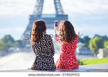 Beautiful twin sisters taking selfie in front of Eiffel Tower while traveling in Paris, France. Happy smiling girls enjoy their vacation in Europe