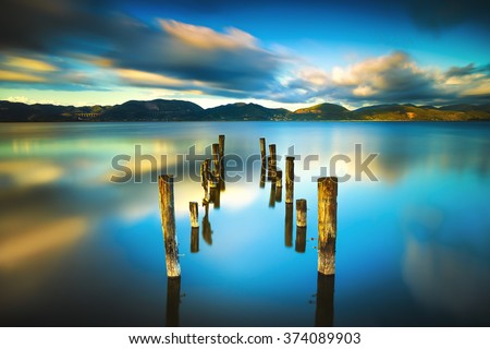 Wooden pier or jetty remains on blue lake sunset and sky reflection water. Long exposure, Versilia Massaciuccoli, Tuscany, Italy.