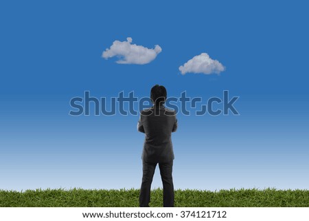 businessman standing on green meadow with blue cloudy sky background