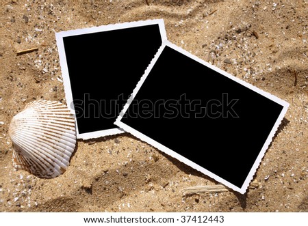 Two blank, black photograph pictures are in the sand and there is a sea shell next to them. Use it for a summer vacation or memory photo at the beach or lake.