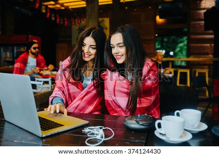 Two young and beautiful girl sitting at the table and looking for something on the Internet
