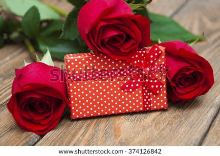 Holiday background. Gift box and beautiful red roses on old wooden background