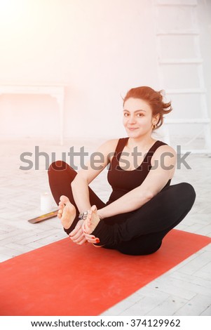 Handsome woman doing yoga practice on red gymnastic carpet in white lit room. Concept of physical and mental health, happy living and well being.