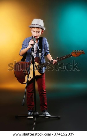 Little boy playing guitar and singing with microphone on a dark lighted background