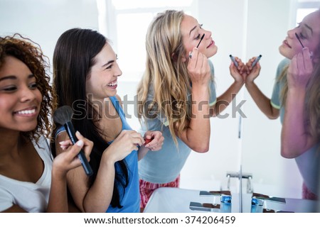Three smiling friends putting makeup on together in the bathroom Royalty-Free Stock Photo #374206459