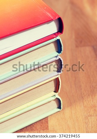 A pile of colorful books on a wooden table. Image has a vintage effect applied.