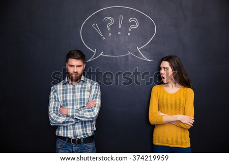 Frowning offended young couple standing with arms crossed after argument over chalkboard background
