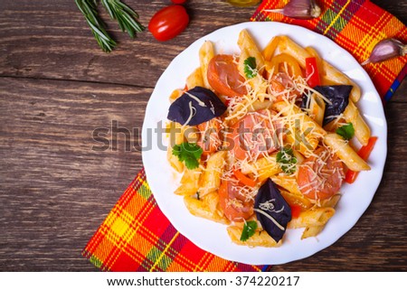 Penne pasta with tomato sauce with sausage, pepper and basil decorated in a plate on a wooden background