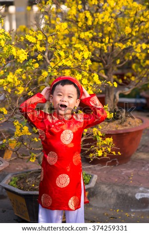 Happy kid having fun with traditional dress (ao dai) in Ochna Integerrima (Hoa Mai) garden. Hoa Mai flower is used for decoration in lunar new year in Vietnam.