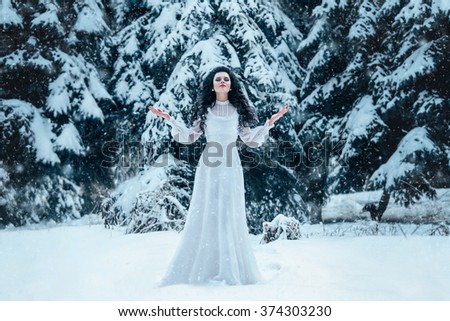 Luxurious brunette young woman in a white vintage old fashion dress standing in a snowy forest, Snow Queen, a fantastic shot, art creative color.Pretty girl got lost froze and prays asks God for help