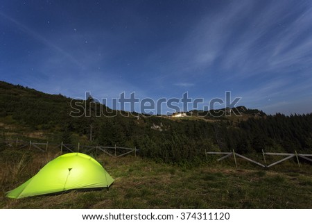 Green illuminated tent in the night with stars and clouds moving in the mountain