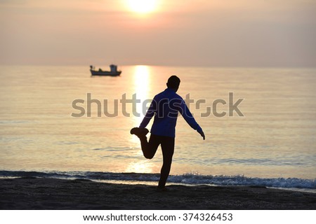silhouette of young sport man stretching leg after running workout outdoors on beach at sunset with orange and purple sky in front of the sea in fitness and healthy lifestyle concept