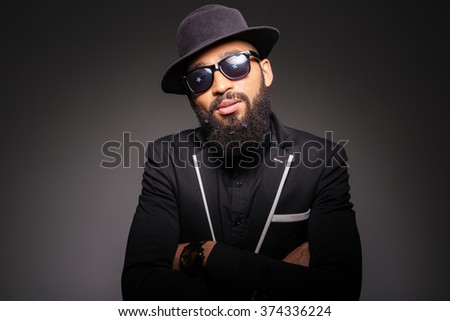 Serious afro american man in fashion cloth and glasses standing with arms folded over black background