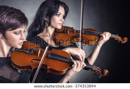 Two beautiful woman playing the violin on a black background