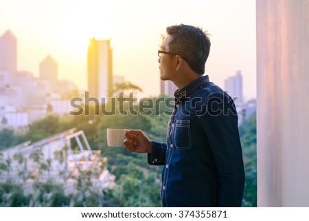 Businessman in denim jacket and glasses drinking hot coffee in sunrise.  Royalty-Free Stock Photo #374355871
