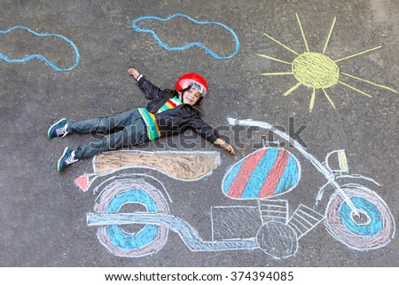 Happy kid boy in race helmet having fun with motorcycle picture drawing with colorful chalks. Children, lifestyle, fun concept. Creative leisture for kids