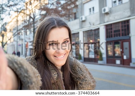 Smiling woman taking a selfie photo in an urban street in winter