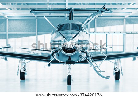Single turboprop aircraft in big hangar. Focus on nose aircraft, colored on technical blue. Royalty-Free Stock Photo #374420176