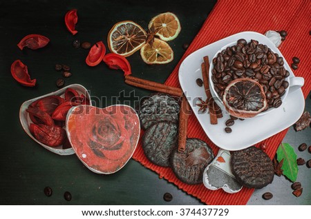 Black table. On a table the casket in the form of heart, a cup with coffee grains and a lemon, chocolate cookies, a Valentine's Day card, red leaflets of the flavored sachet, 