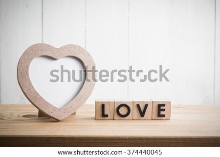 Heart shaped photo frame with "love" in cube on wood table