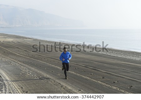 young sport man running alone on desert beach along the sea shore training workout on a foggy and overcast winter early morning in fitness and healthy lifestyle concept