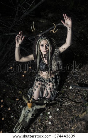portrait of Beautiful woman with long dreadlocks hair sit near cow skull with horns against wild forest trees Young girl pray satan Woman shaman in ritual garment wear fur and leather clothes