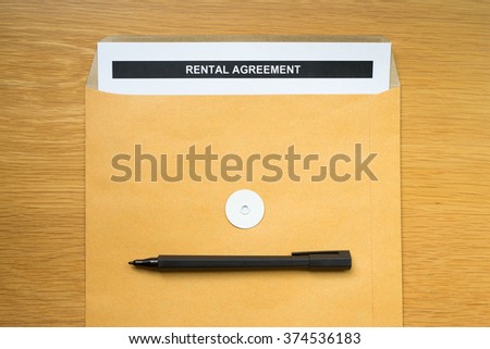"Rental Agreement" paper in brown envelope with black pen on wood table background.