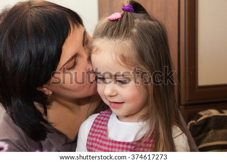 Mom whispers little daughter a secret into the ear. Pretty girl smiling
