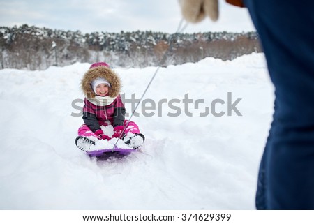 childhood, sledding, leisure, season and people concept - parent carrying happy little kid on sled in winter