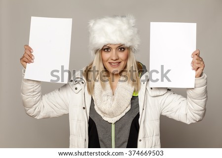 smiling girl in winter clothing holding two blank sheets of paper