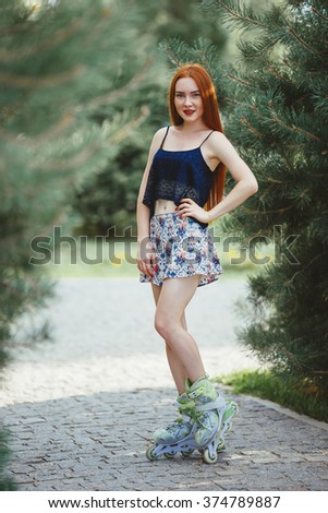 red-haired woman in roller skate in a city park on her T-shirt and bright blue chert in the park grow spruce lined road pavement