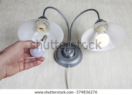 Replacing the bulbs in wall lights, hand holds a LED lamp.