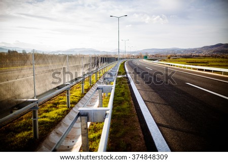 Freeway on a sunny day trough scenic green meadows.Motorway traveling long distance.Asphalt highways road in rural scene use land transport and traveling concept.Vehicular traffic.Fence.Highway bumper