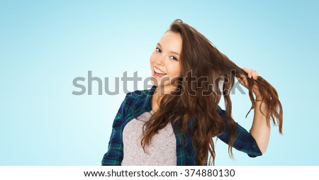 people, hair care, style and teens concept - happy smiling pretty teenage girl holding strand of her hair over blue background