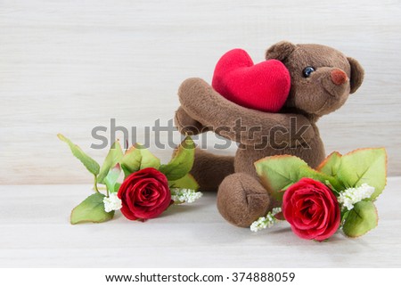Single Teddy bear holding a heart-shaped pillow with plank wood board background.In Valentine Day.