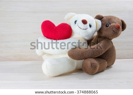 Couple Teddy bear holding a heart-shaped pillow with plank wood board background.In Valentine Day.
