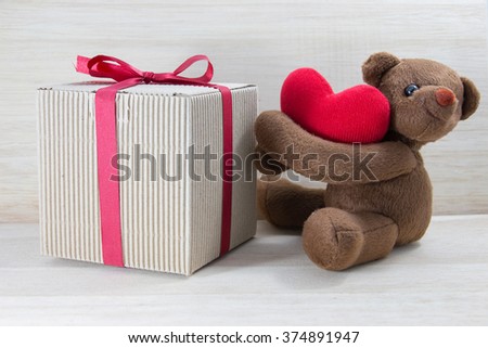 Teddy bear holding a heart-shaped pillow and gift box with plank wood board background.In Valentine Day.