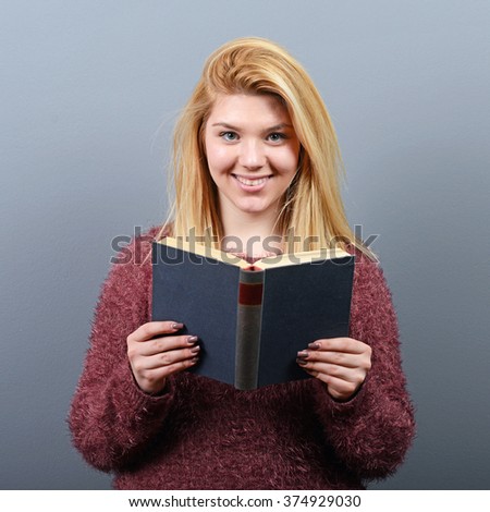 Portrait of young woman reading book against gray background