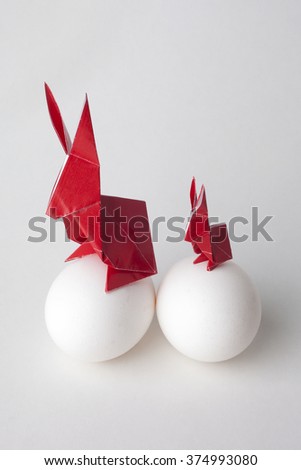 Red origami Easter bunny rabbits sitting on a white eggs.