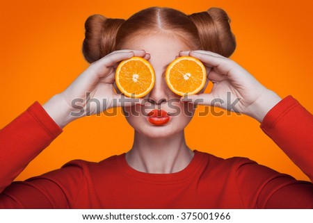 Young beautiful funny fashion model with orange slice on background. with makeup and hairstyle and freckles.  Royalty-Free Stock Photo #375001966