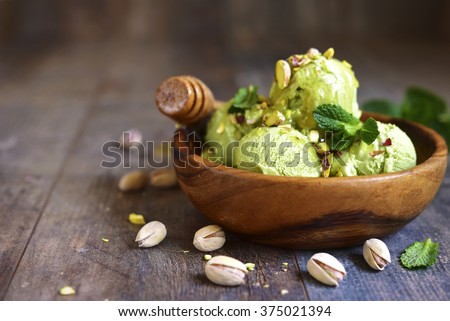 Pistachio ice cream with chopped nuts and honey on a rustic background.