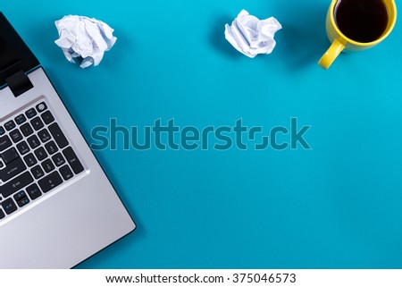 Office table desk with set of colorful supplies, white blank note pad, cup, pen, pc, crumpled paper, flower on blue background. Top view and copy space for text