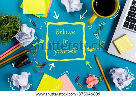 Believe in yourself. Office table desk with supplies, white blank note pad, cup, pen, pc, crumpled paper, flower on wooden background. Top view
