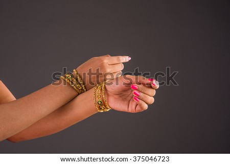 Indian Jewellery - Closeup of girl wearing traditional designer gold bangles/bracelets and showing graceful dance poses of hand over dark background, selective focus