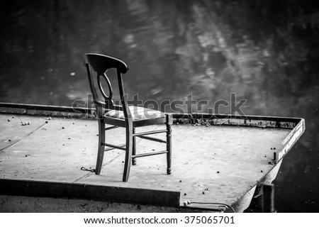 Black and white photography of lonely chair on a floating bridge at lake at evening. Lonely chair on pontoon near water. 