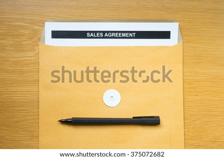 "Sales Agreement" paper in brown envelope with black pen on wood table background.
