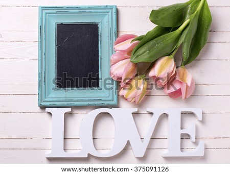 Fresh  spring  pink  tulips, word love and empty blackboard  on white  painted wooden background. Selective focus. Place for text. 