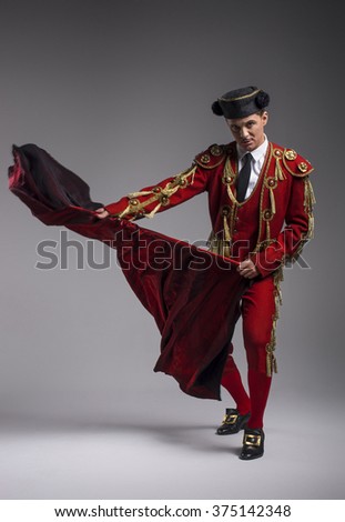 Studio shot of man dressed as Spanish torero, matador, bullfighter. Performing a traditional classic bullfight, standing and holding the capote. Royalty-Free Stock Photo #375142348