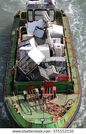 Photo seen from above of sea open hopper barge full of used domestic appliances recycling material garbage riding on blue waves water splashes on seascape background, vertical picture 