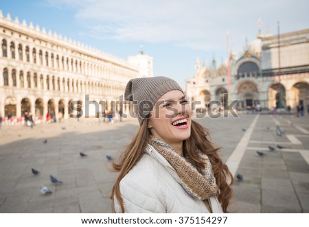 Take classical tourist enjoyment in Venice, Italy - wander over San Marco square, chase pigeons and take photos. Laughing young woman standing on Piazza San Marco having fun time